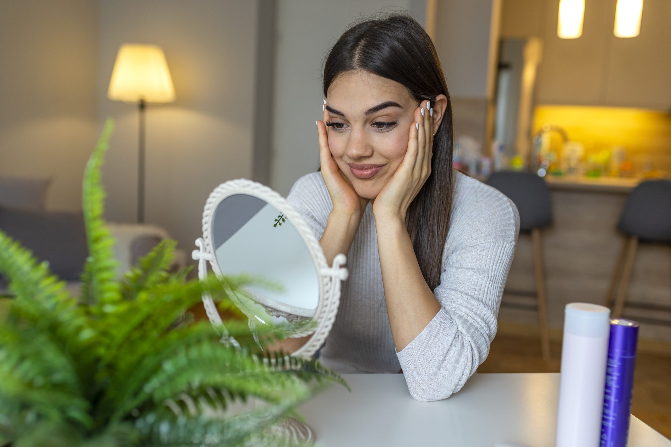 Facial Beauty. Portrait Of Sexy Young Woman With Fresh Healthy Skin Looking In Mirror Indoors. Closeup Of Beautiful Smiling Girl With Natural Makeup Touching Face. Cosmetic Concept. High Resolution